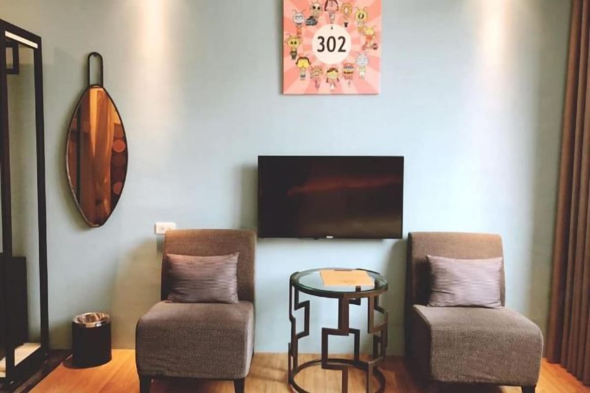 A room with two armchairs, a small round table, a television mounted on the wall, and a decorative piece with the number 302.
