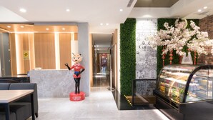 A hotel lobby with a reception desk, a statue, a glass display case, and a green wall with illustrations. - Tianli Hotel (Tainan)
