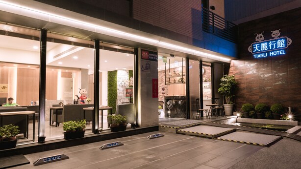 A hotel entrance with a reception desk, indoor seating area, and a small outdoor garden with potted plants. - Tianli Hotel (Tainan)