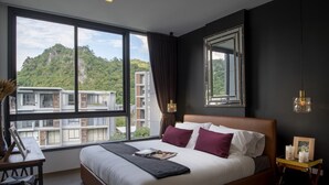 A modern bedroom with a large bed, a view of buildings and greenery, and a window with curtains.