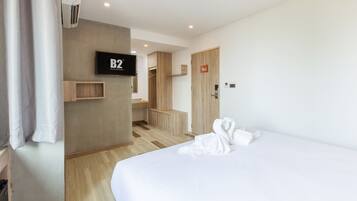 Habitación de hotel con una cama, un televisor montado en la pared, un armario de madera, un pequeño mueble de madera y una toalla sobre la cama.