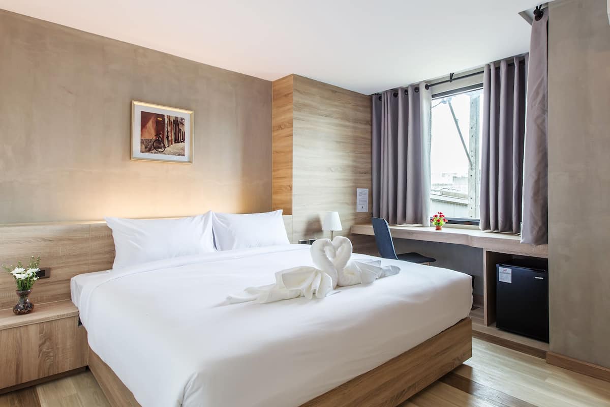 A hotel room with a large bed, a desk, a window with curtains, and a wall-mounted air conditioner.