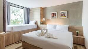 A hotel room with two beds, a large window with curtains, wooden paneling, a wall-mounted lamp, and two framed pictures. - B2 Ubon Premier Hotel (Ubon Ratchathani)