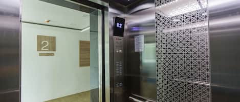 An elevator interior with a digital display showing the number 2, a Sigma brand elevator control panel, and a decorative metal mesh panel.