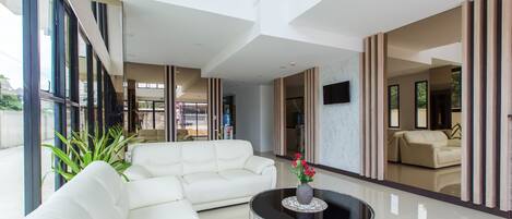 Un amplio salón con un sofá blanco, una mesa de centro redonda de cristal y un televisor montado en la pared.