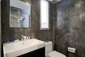 A bathroom with a white sink, mirror, and toilet against a textured wall. - Condo Studio B at Replay E305 (Koh Samui)