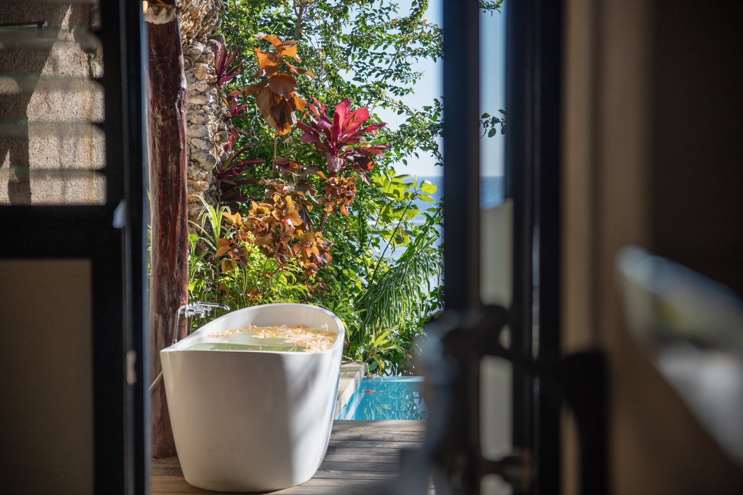 A view through a doorway to a pool area with a white tub and a stone wall.