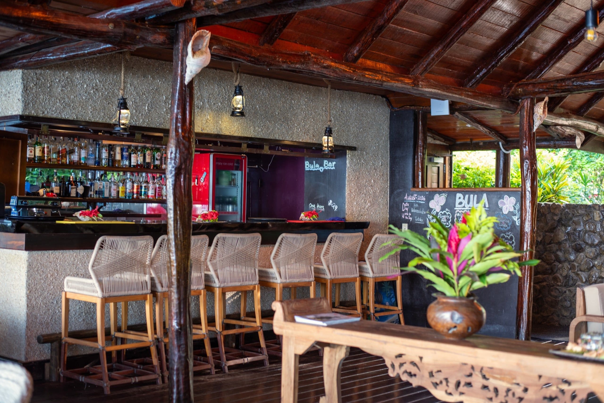 Un espace bar avec des chaises en bois, un comptoir bien garni de différentes bouteilles et un menu écrit à la craie.