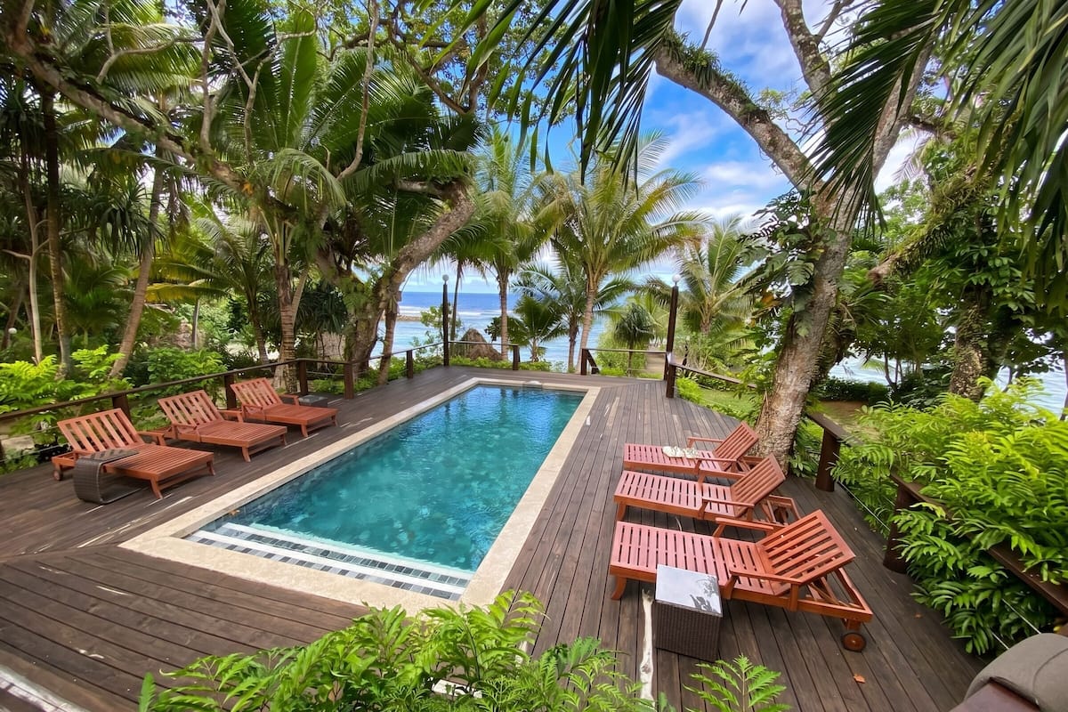 Une terrasse en bois avec une piscine, des chaises longues et une végétation tropicale.