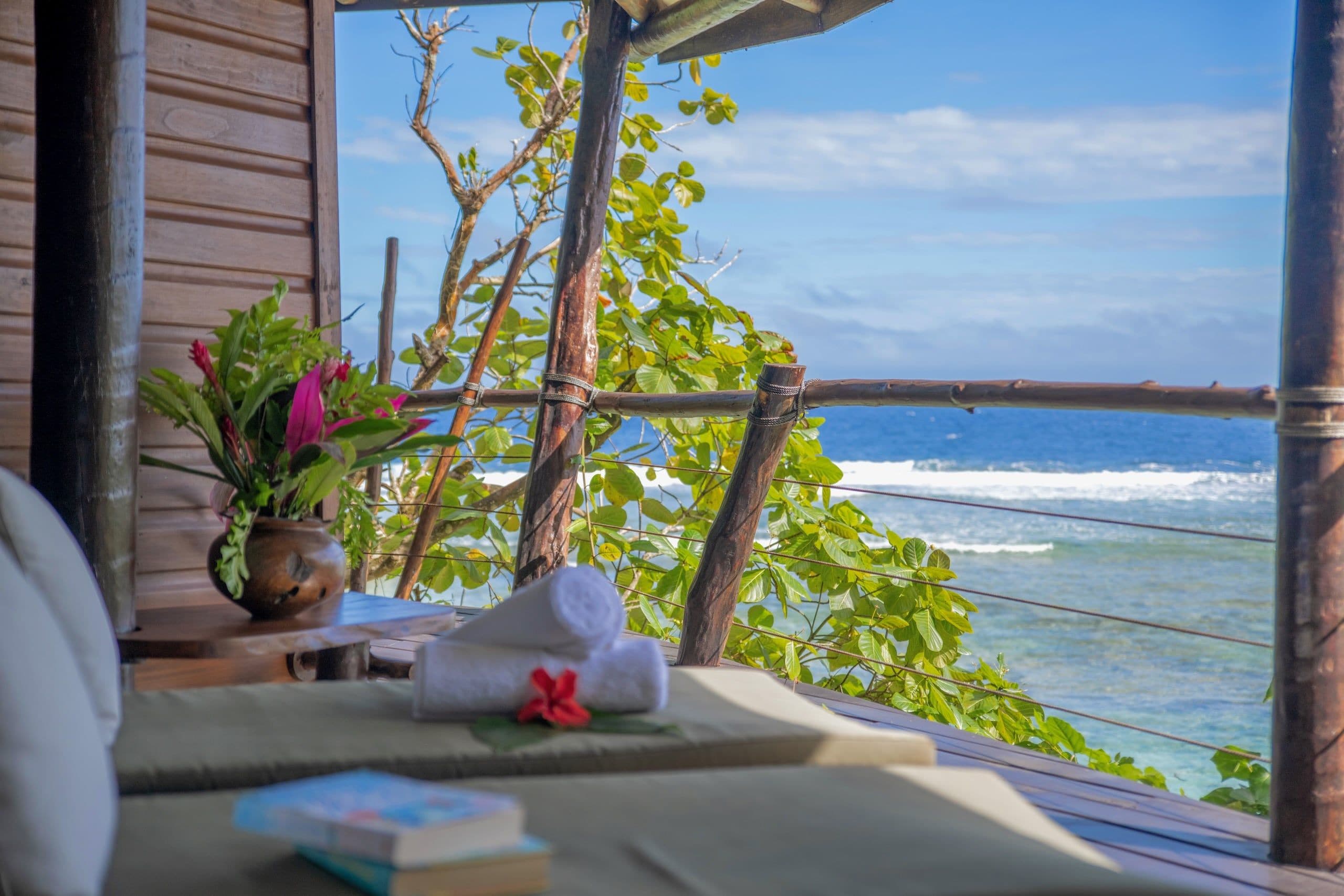 A seaside view from a wooden deck with a view of the ocean, a towel, and a book.