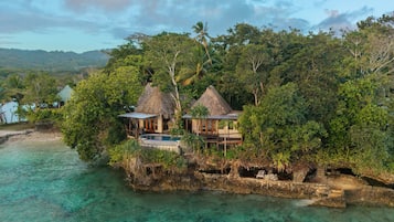 A tropical island resort with thatched-roof cottages, a swimming pool, and lush greenery.