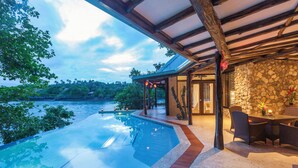 A poolside area with a stone wall, wooden pergola, and a dining table with chairs. - Savasi Island Resort (Savusavu)