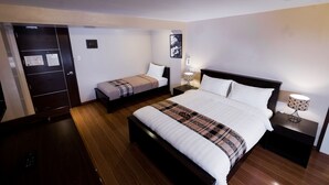 Une chambre d’hôtel avec un grand lit, un lit plus petit, une armoire et un bureau avec une lampe.