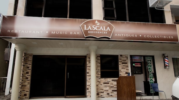 La façade d’un immeuble porte une enseigne indiquant « Lascalá Residences », et abrite un restaurant, un bar musical, ainsi qu’une boutique d’antiquités et d’objets de collection.