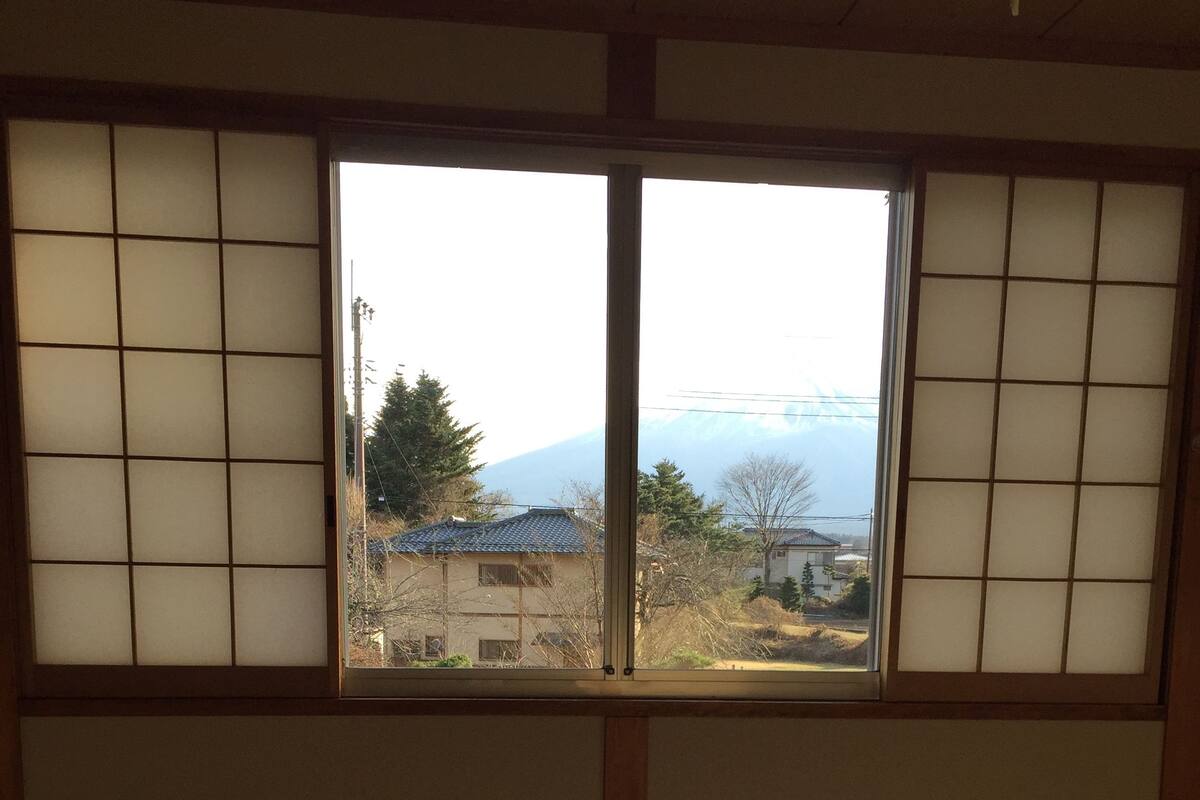 Une pièce avec un lit, une fenêtre dotée de panneaux coulissants japonais et une vue sur une montagne.