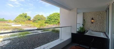 A balcony with a view of a garden and trees, a stone wall, and a seating area with a table and chairs.
