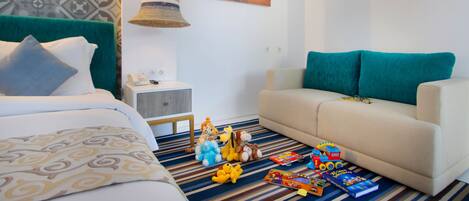 Une chambre d’hôtel avec un lit, un canapé, un mur décoré d’un motif, une image de plage et des jouets sur le sol.