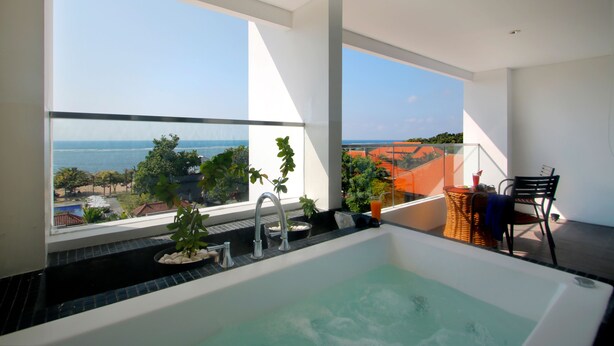 Une salle de bain moderne dotée d’une grande baignoire, d’une fenêtre donnant sur la mer et d’une petite table avec une chaise.
