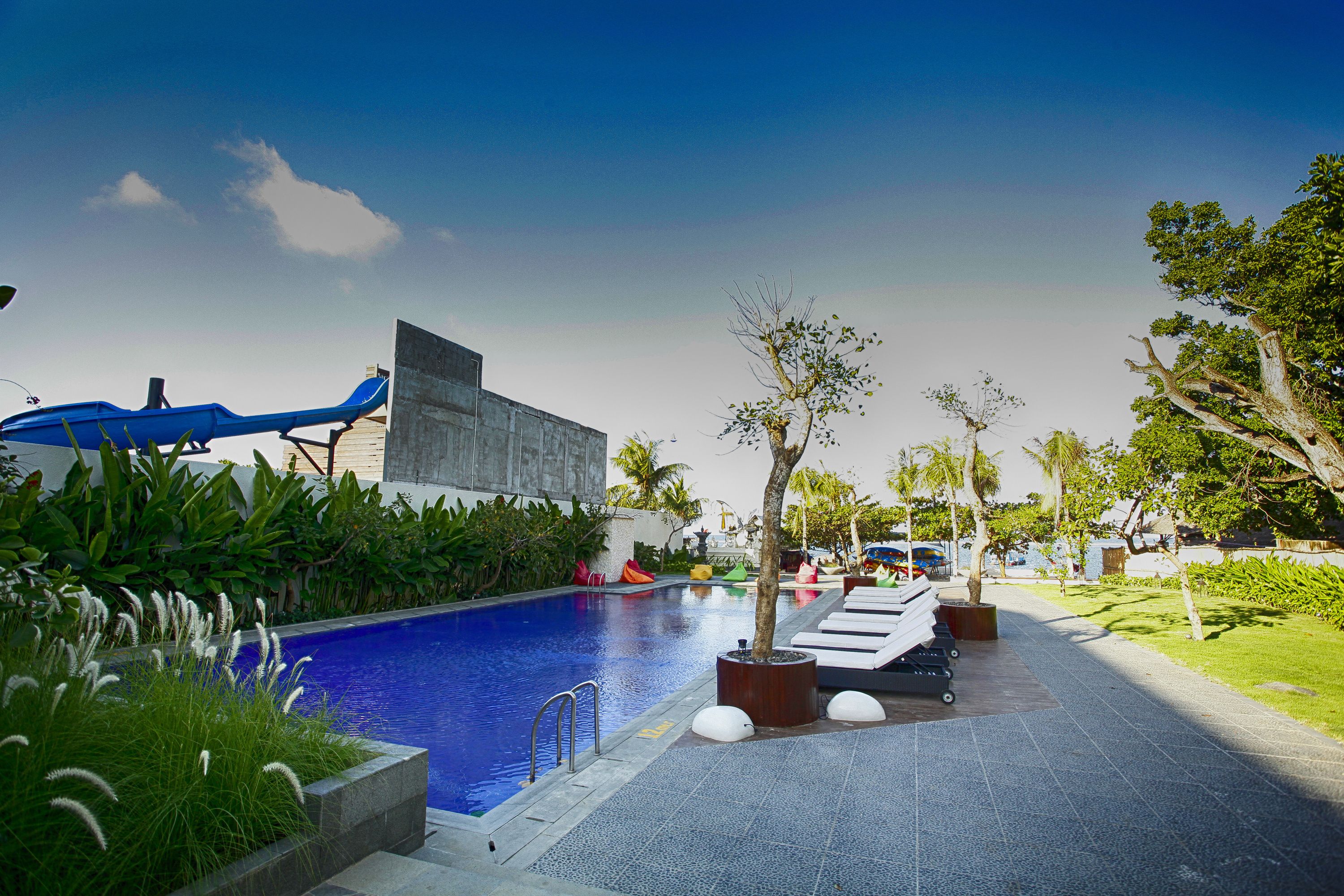 A swimming pool with lounge chairs, a water slide, and a modern building.