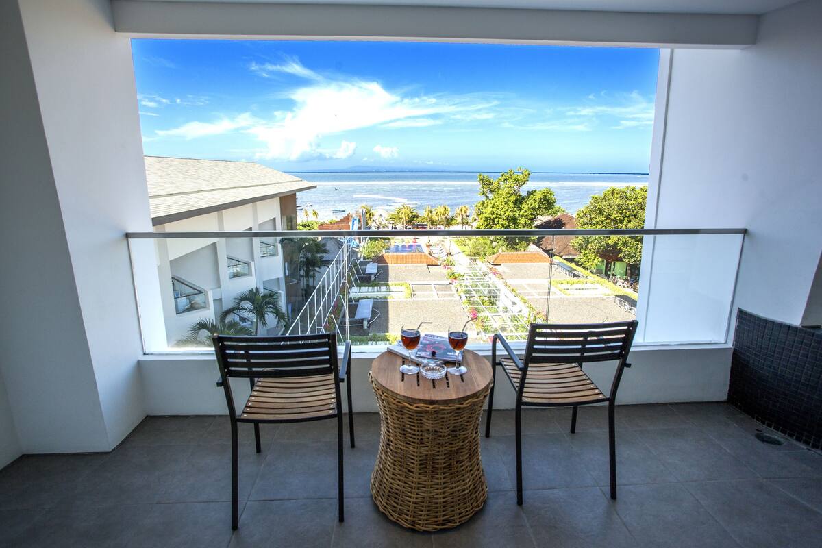 Ein Balkon mit Meerblick, zwei Korbstühle und ein Tisch mit Getränken.