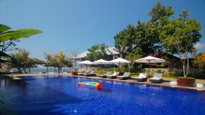 Une piscine entourée de verdure, avec des chaises longues et des parasols, offrant une vue sur la mer.