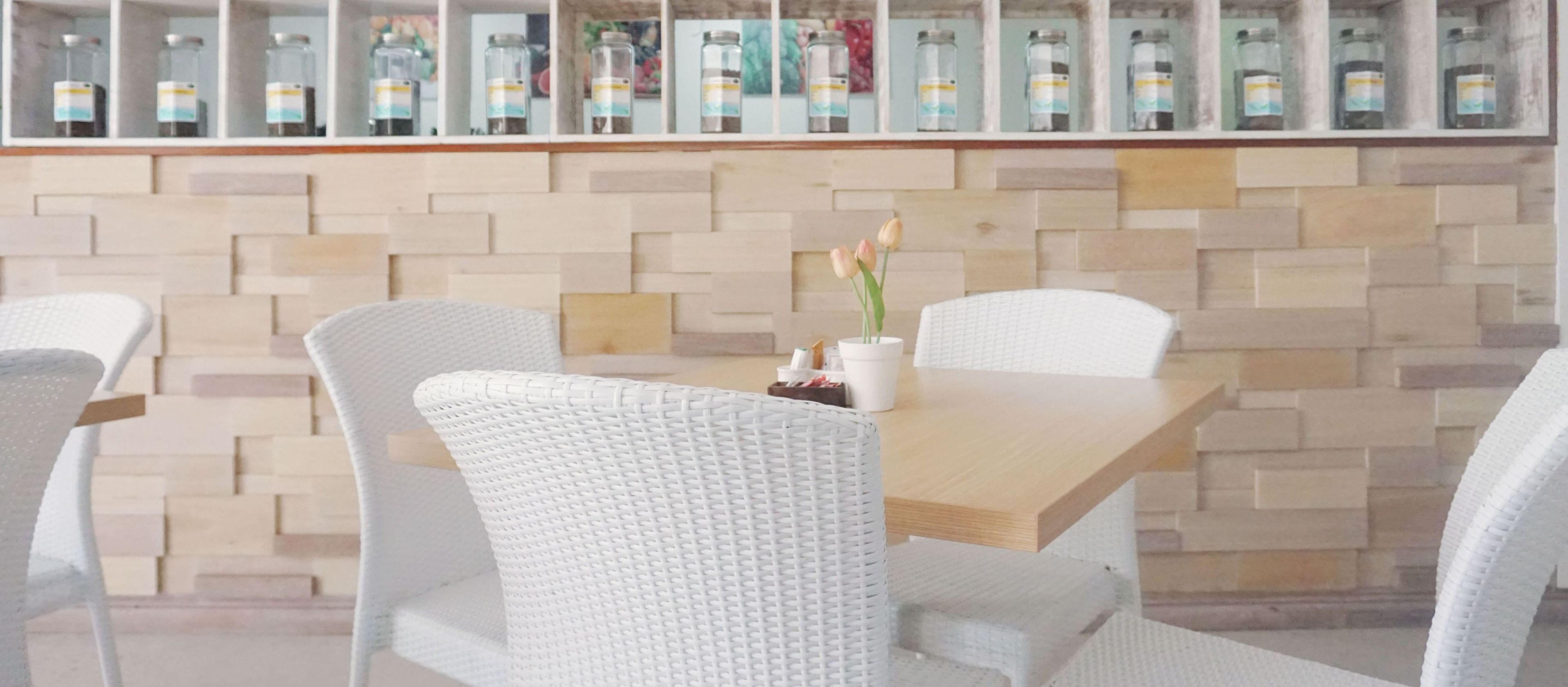 A dining area with a wooden table and white chairs, a vase with flowers, and a wall with jars.