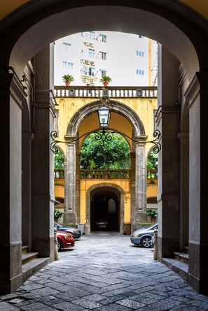 An arched passageway with a cobblestone floor, flanked by buildings with balconies and potted plants. - Sarracino Relais (Naples)