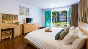 A hotel room with a bed, a desk with a television, and a window with a view of greenery. - Baan San Ploen Condominium by Renvio (Hua Hin)