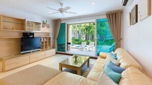 A modern living room with a sofa, coffee table, TV, and shelves. - Baan San Ploen Condominium by Renvio (Hua Hin)