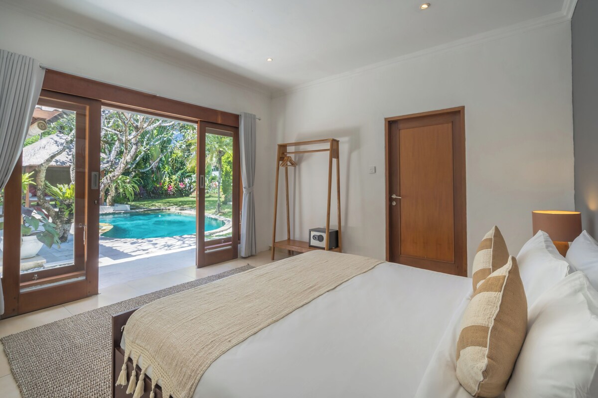 A bedroom with a bed, a wooden wardrobe, a hanging chair, and a view of a swimming pool.