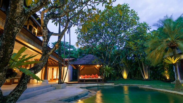 Un complexe hôtelier doté d’une piscine, d’un espace de détente couvert avec des coussins et d’une végétation tropicale luxuriante.
