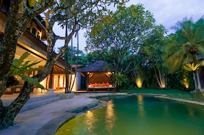 A resort with a swimming pool, a covered seating area with cushions, and lush tropical vegetation. - The Jasmina Estate (Seminyak)
