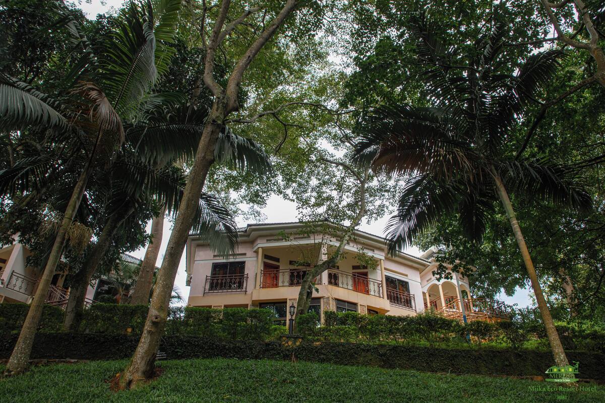 A two-story building with balconies, surrounded by lush greenery and palm trees.