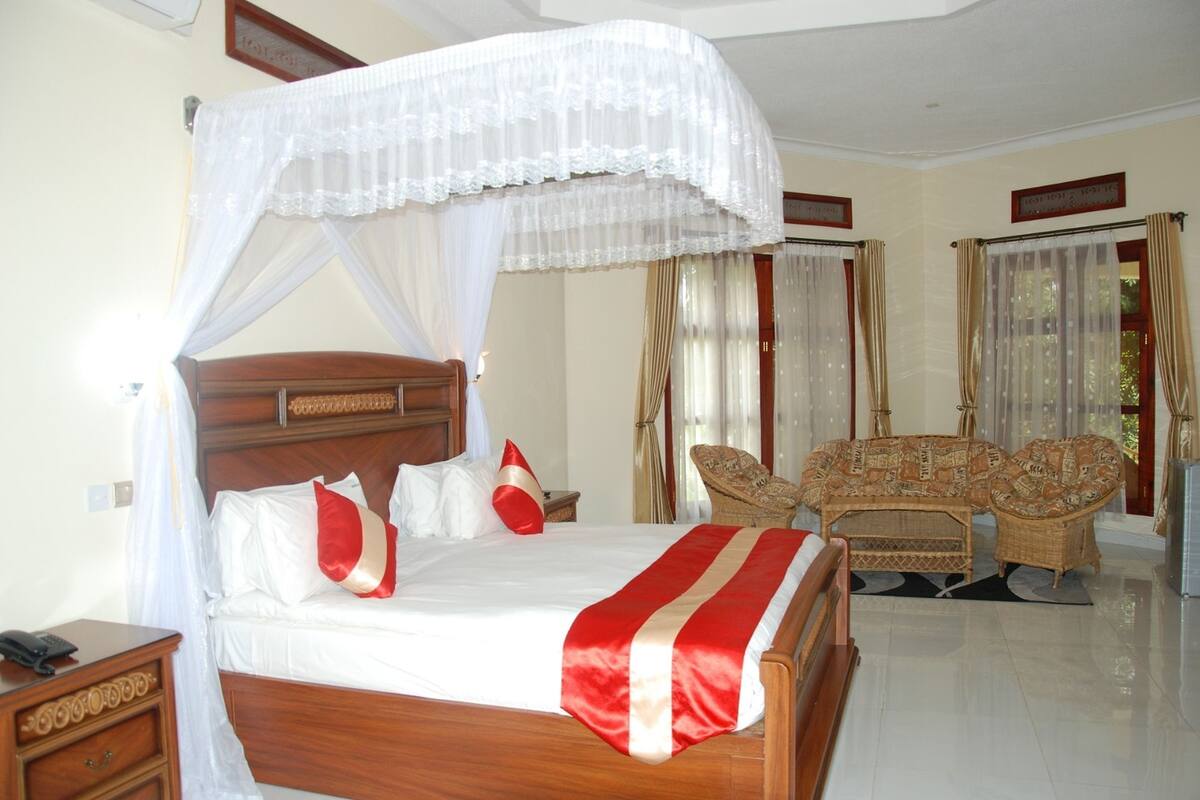 A bedroom with a four-poster bed, a wooden nightstand, a wicker sofa, and a small table.