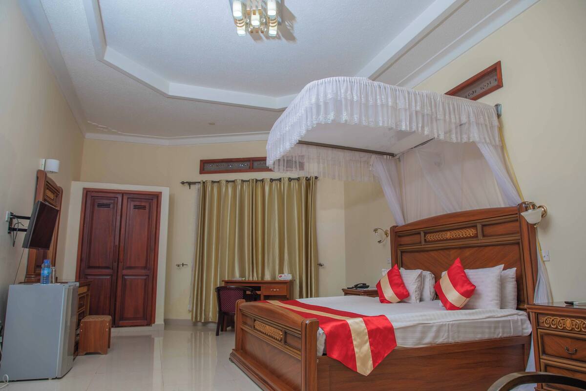 A hotel room with a wooden bed, a desk, a chair, a wardrobe, and a television.