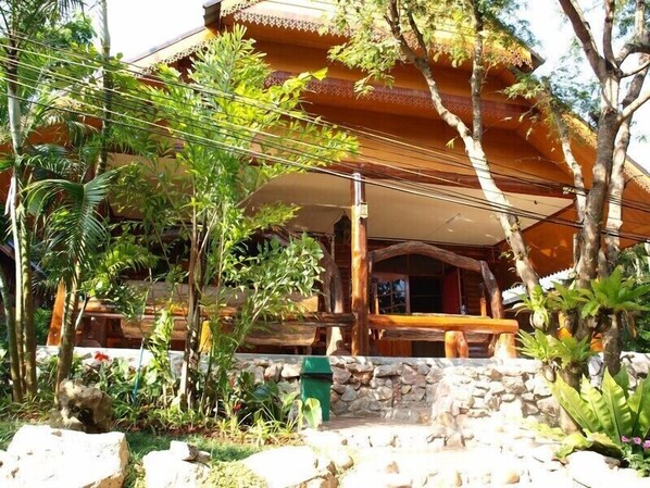 Un edificio tradicional de madera con base de piedra, rodeado de vegetación tropical.