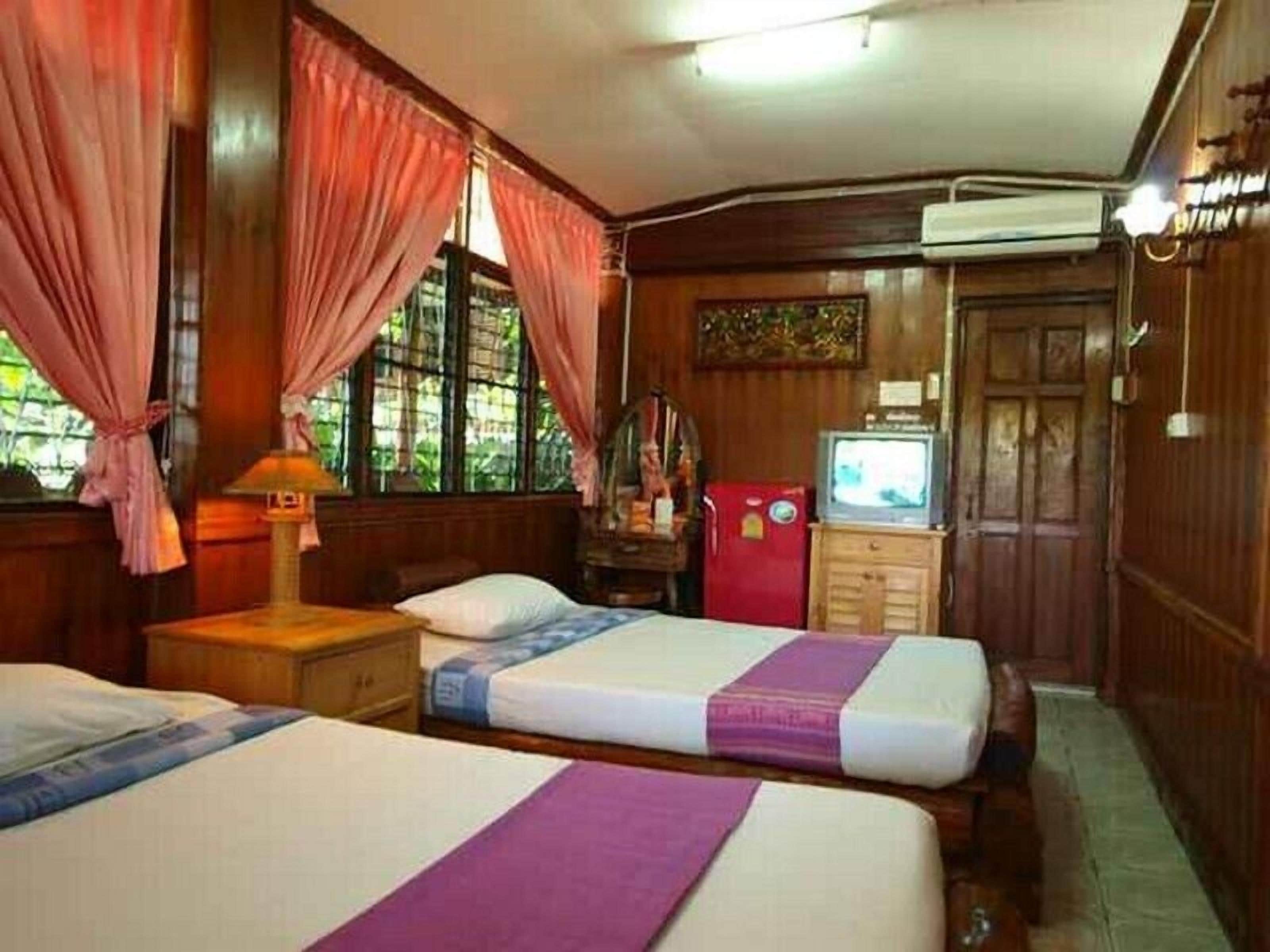 A room with two beds, a television, a wardrobe, and a window with curtains.