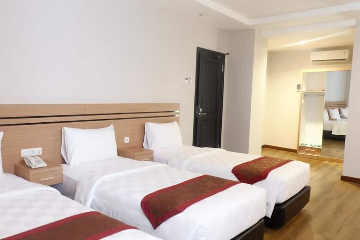 A hotel room with three beds, a wooden headboard, a bedside telephone, and a mirror.