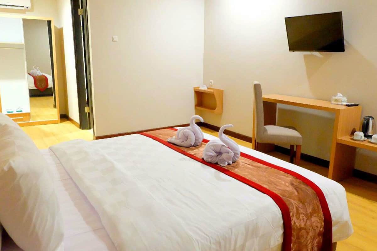 A hotel room with a bed, a desk, a chair, a TV, and a mirror.
