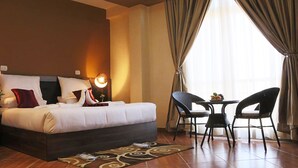 A hotel room with a bed, two chairs, a small table, and a lamp. - Heyday Hotel (Addis Ababa)