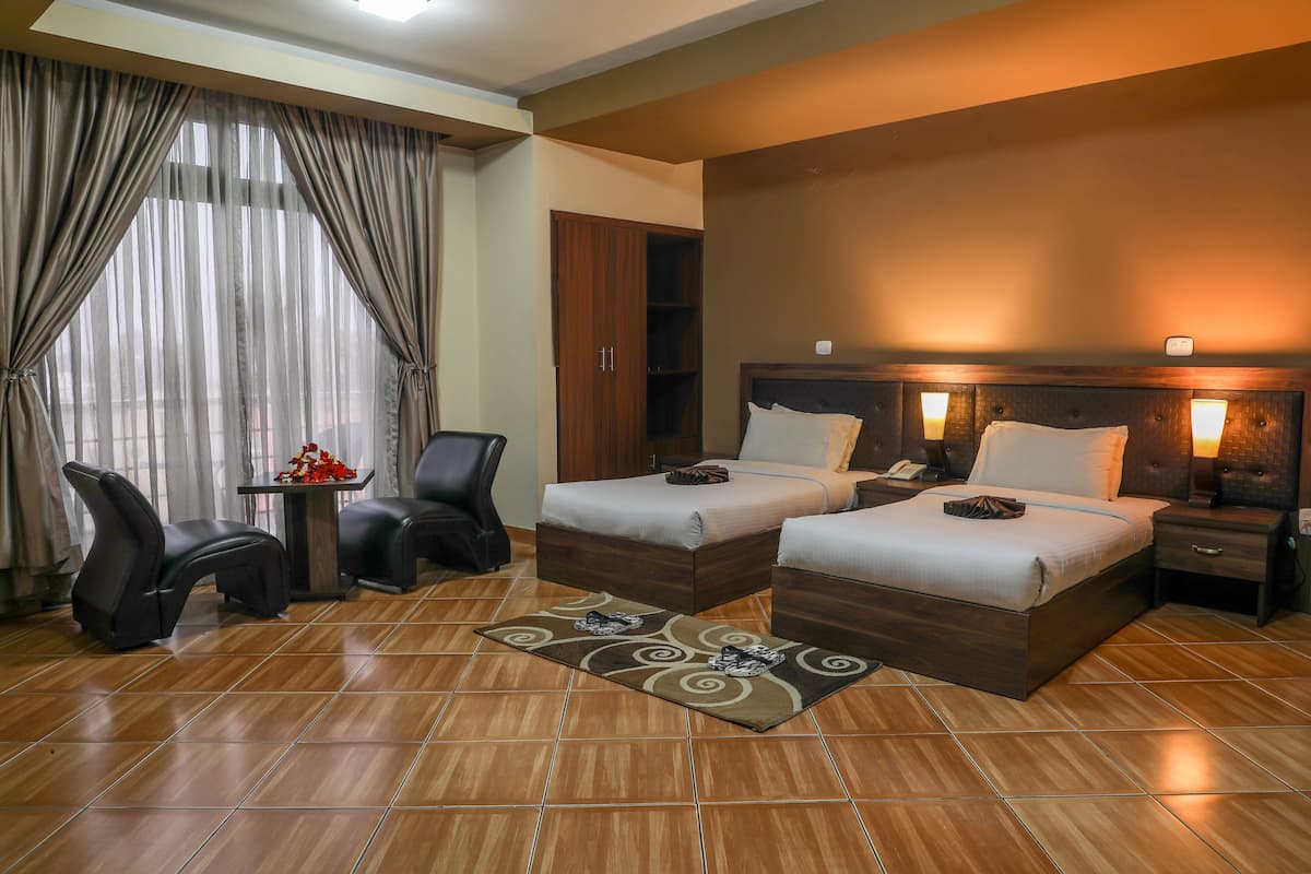 Habitació d'hotel amb dos llits, un escriptori, una cadira i una finestra gran amb cortines.