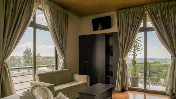 A hotel room with a sofa, a coffee table, a flat-screen TV, and a large window with curtains. - Heyday Hotel (Addis Ababa)
