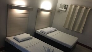 Habitación de hotel con dos camas individuales, una mesita de noche con una toalla y una botella, un aire acondicionado de pared y una cortina.