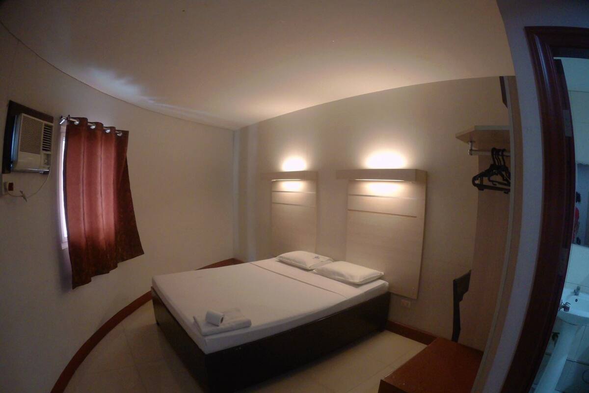 A hotel room with a single bed, a bedside table, a mirror, and a bathroom with a sink and toilet.