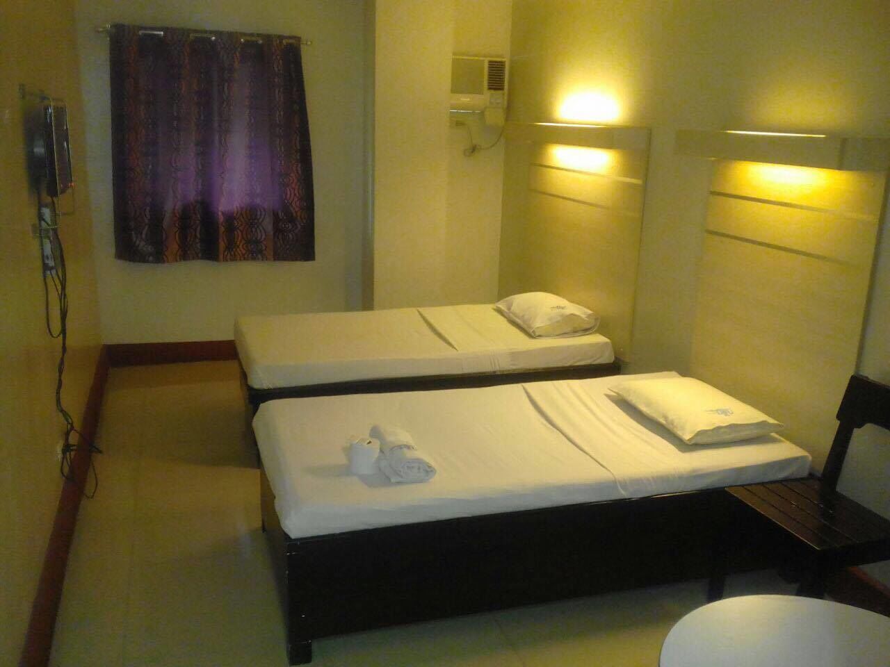 Una habitación de hotel pequeña con dos camas individuales, una mesita de noche, una silla, una cortina y un calentador fijado a la pared.