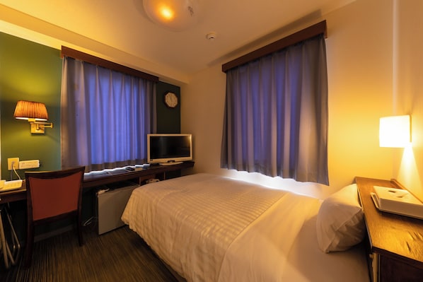 Una habitación de hotel con cama, escritorio, silla, televisor y cortinas.