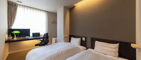 A hotel room with two beds, a desk with a computer, a lamp, and a window with curtains.