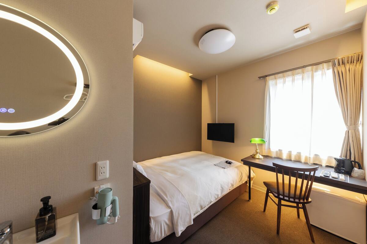 A hotel room with a bed, desk, chair, TV, and a mirror.