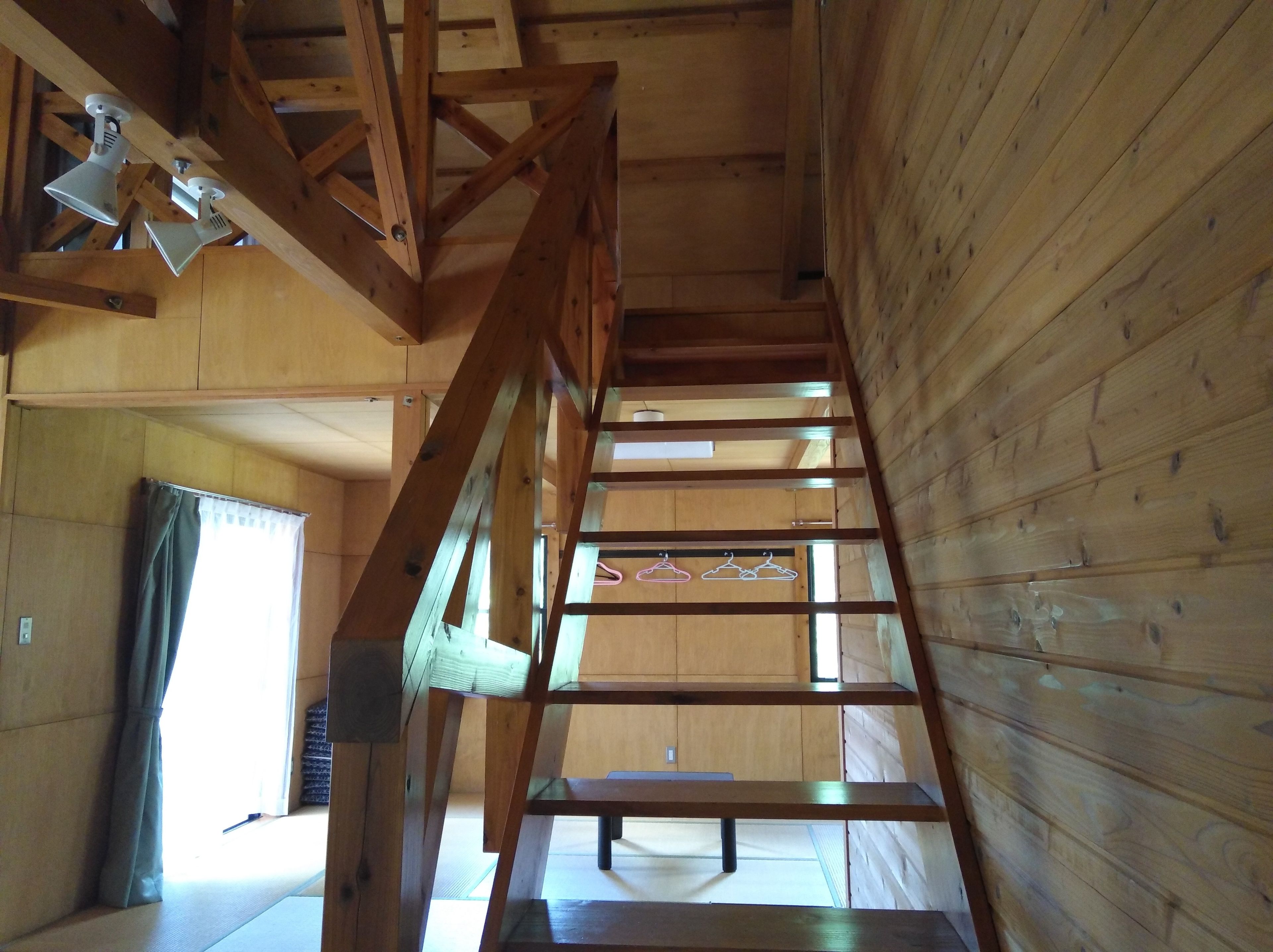 A wooden interior with a staircase, wooden beams, and a window with a curtain.