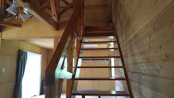 A wooden interior with a staircase, wooden beams, and a window with a curtain.